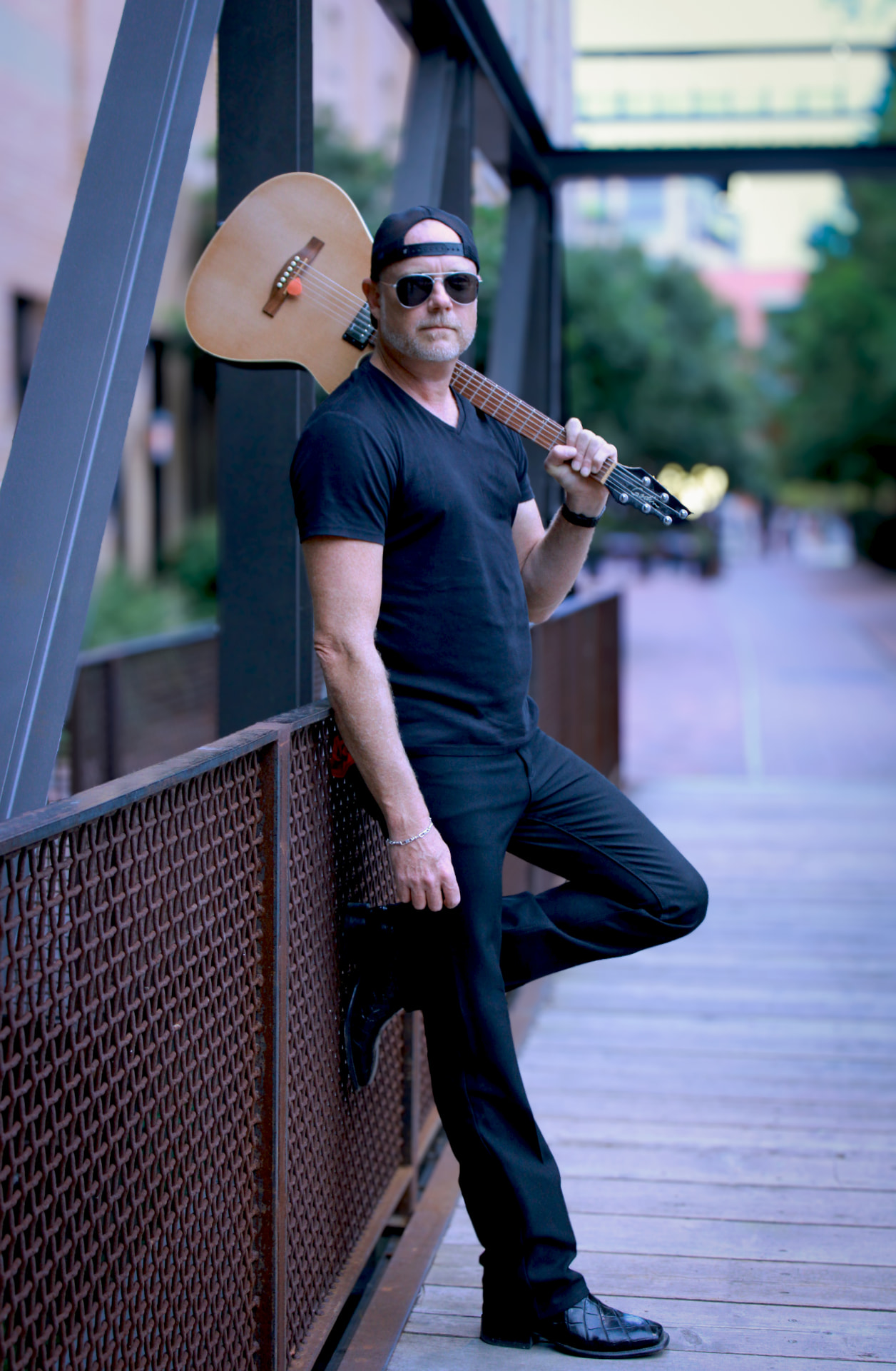 Whiskey Bravo leaning on a bridge railing with his guitar over his shoulder